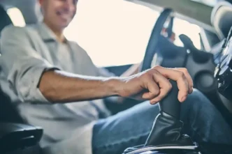 Motorista sorridente trocando a marcha de carro, com a mão na alavanca de câmbio dentro do veículo.