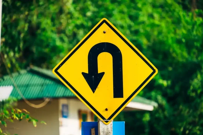 Placa de trânsito amarela indicando retorno em curva acentuada em uma estrada arborizada