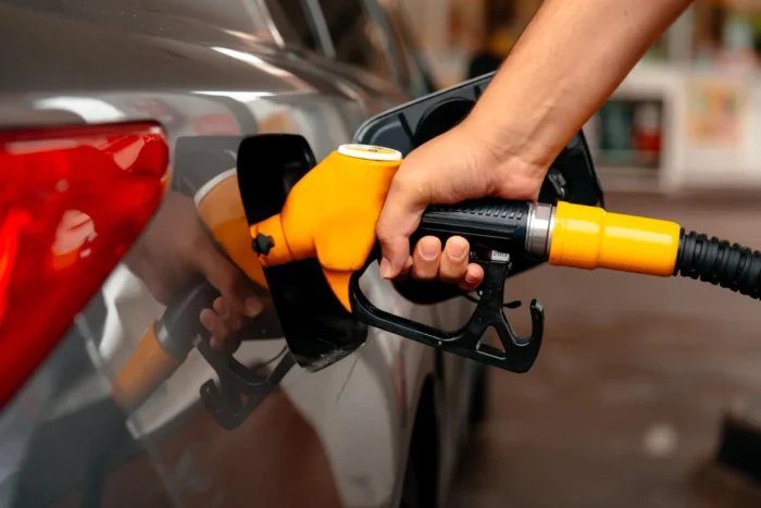 Mão abastecendo carro com bico de combustível enquanto avalia escolha entre álcool ou gasolina