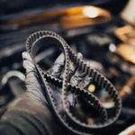Mão com luva segurando correia dentada automotiva próxima ao motor do carro