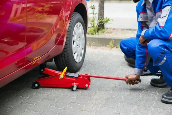 Profissional utilizando um macaco de carro para erguer um veículo vermelho durante manutenção ou troca de pneu.