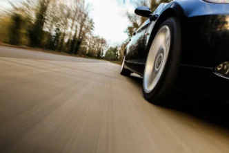 Carro em alta velocidade visto de baixo, com efeito de movimento na pista; contexto de multa por excesso de velocidade.