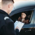 Motorista sem habilitação recebendo autuação de agente de trânsito à janela do carro, ilustrando a situação de multa por dirigir sem habilitação e suas consequências.