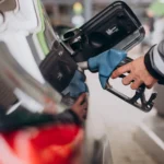 Reabastecimento de combustível em posto, com frentista abastecendo carro através da bomba, destacando mangueira e bico de gasolina.