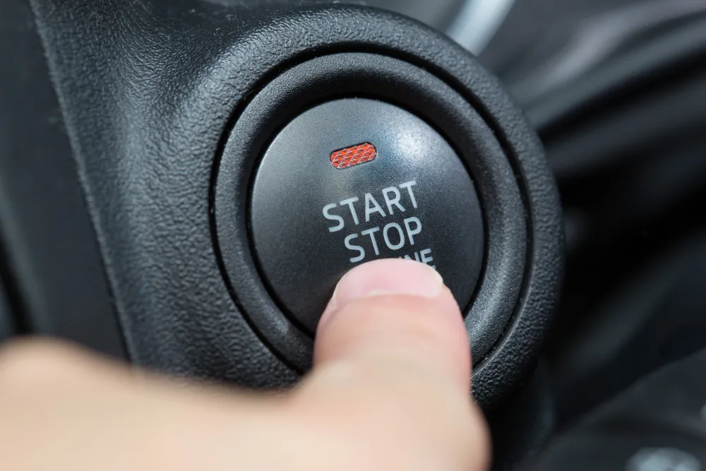 Close do botão start-stop de um carro sendo pressionado por um dedo, com luz indicadora vermelha acesa