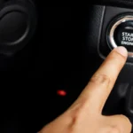 Dedo apontando para o botão start-stop cromado no painel escuro de um carro