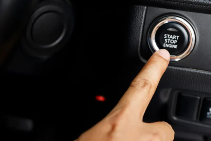 Dedo apontando para o botão start-stop cromado no painel escuro de um carro
